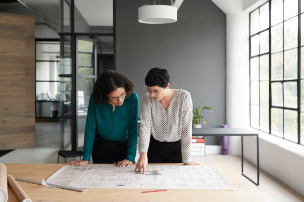 Businesswomen working with blueprint while standing by table in office