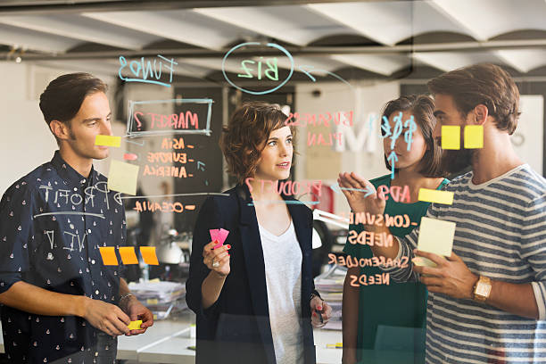 Business people discussing over business plan on glass wall in office