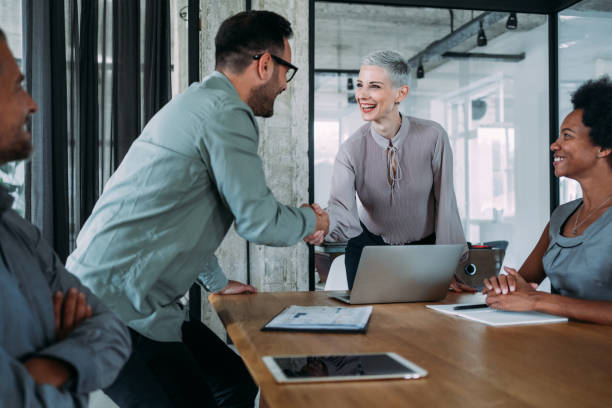 Entrepreneurs handshaking during a meeting with their colleagues in the office. Business persons shaking hands on a meeting in board room.